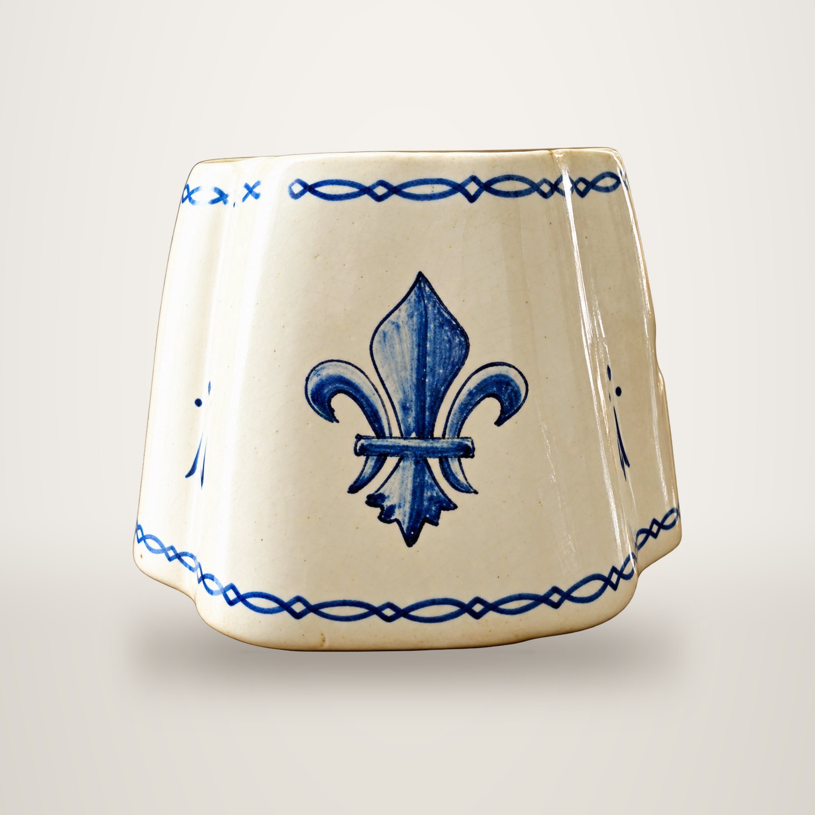 Un abat-jour crème orné d'une fleur de lys bleue au centre et de frises bleues sur les bords, photographié sur fond blanc.
