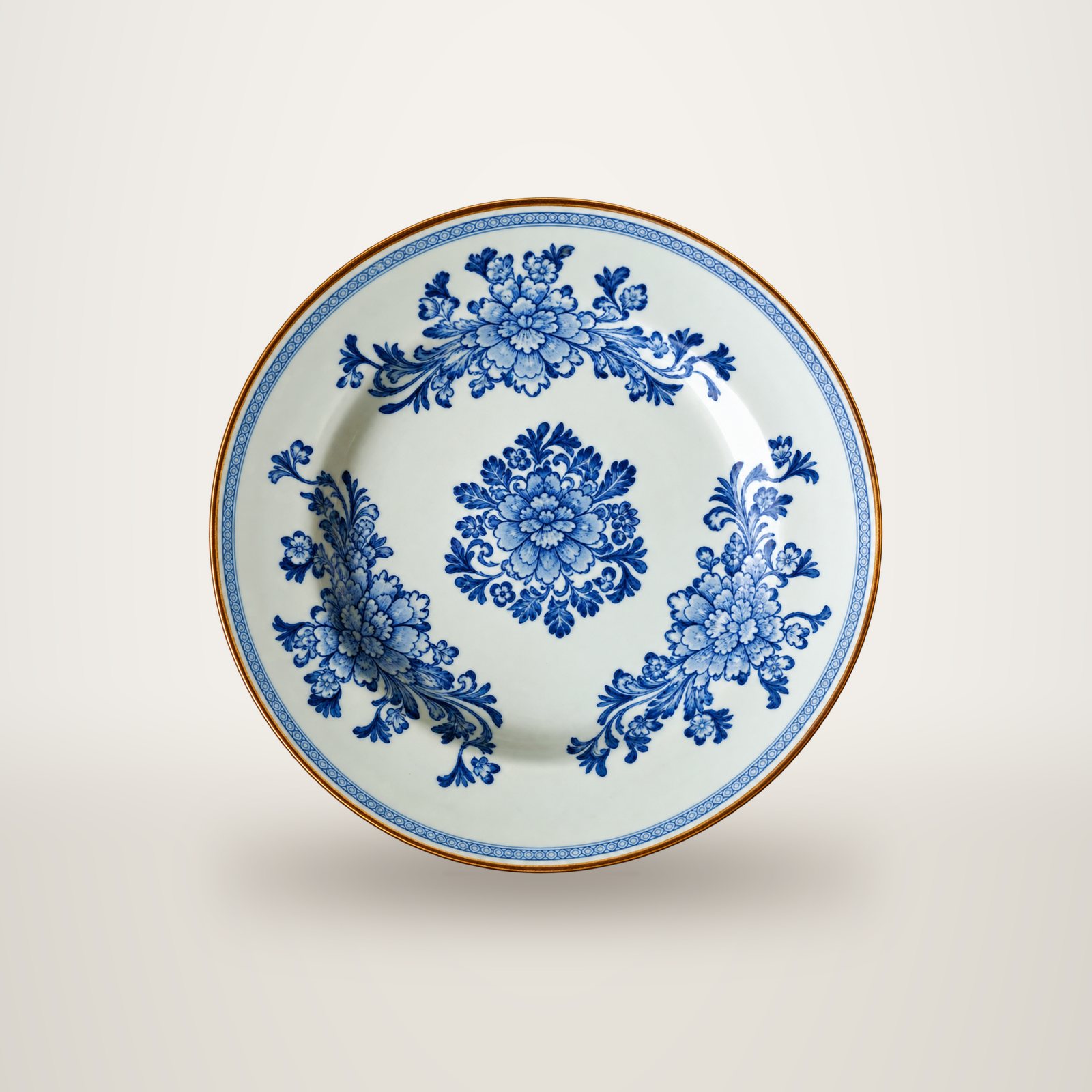 Une assiette ancienne en céramique blanche ornée de motifs floraux bleus, photographiée seule sur un fond blanc uni.