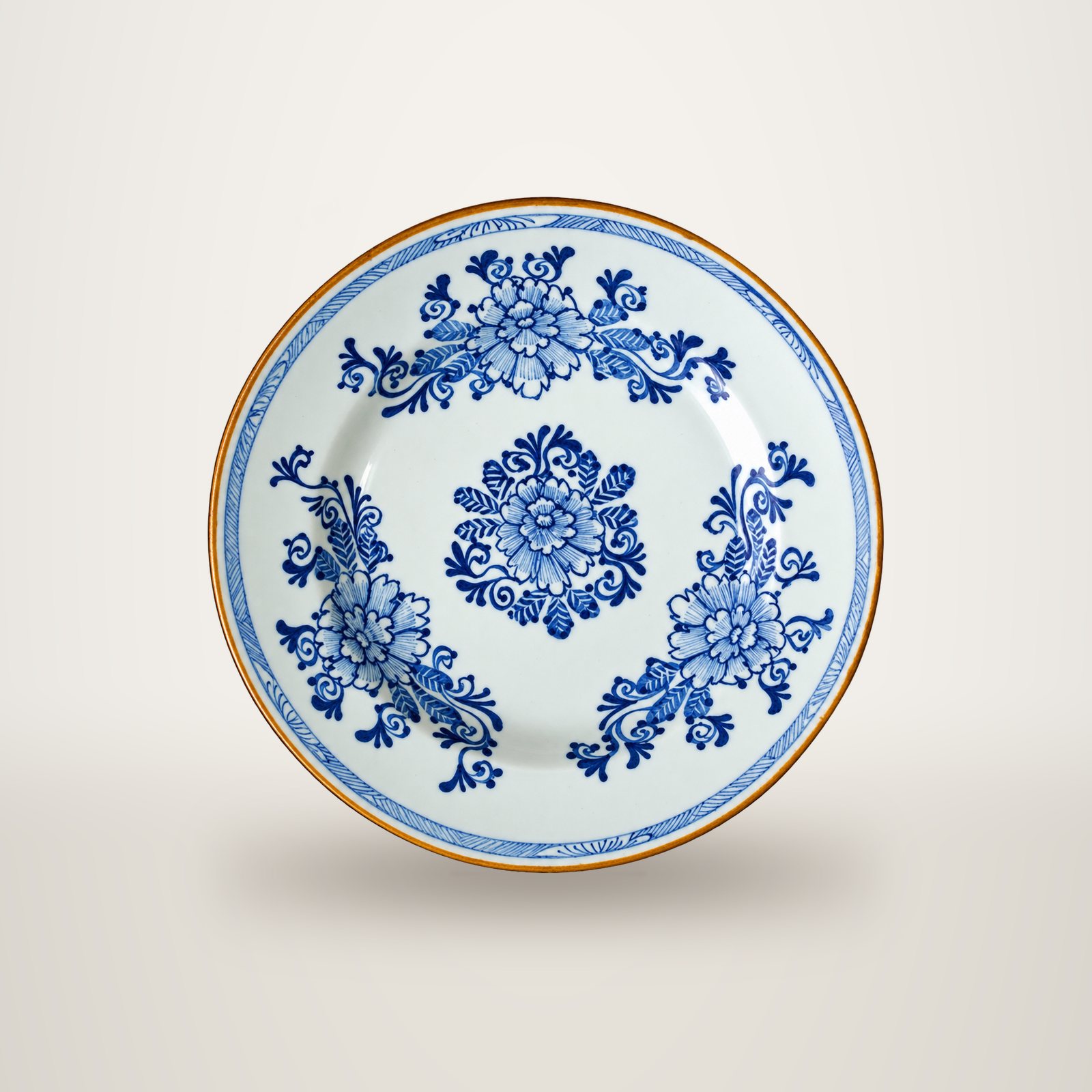 Assiette ancienne en faïence blanche à motifs de fleurs bleues, au bord orné d'un liseré brun doré, photographiée sur fond blanc.