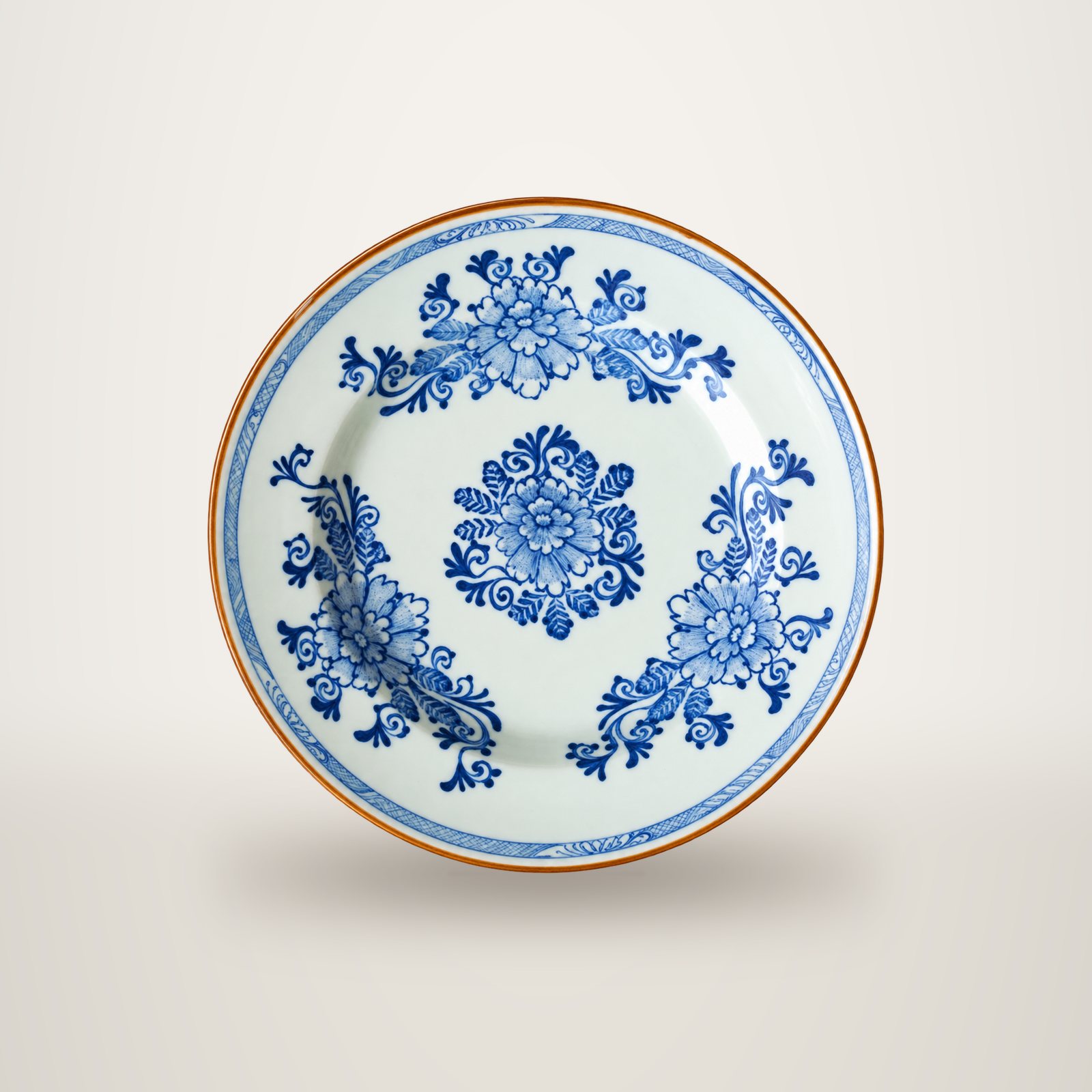 Assiette ancienne en faïence blanche ornée de motifs floraux bleus et d'un bord brun, photographiée de dessus sur fond blanc.