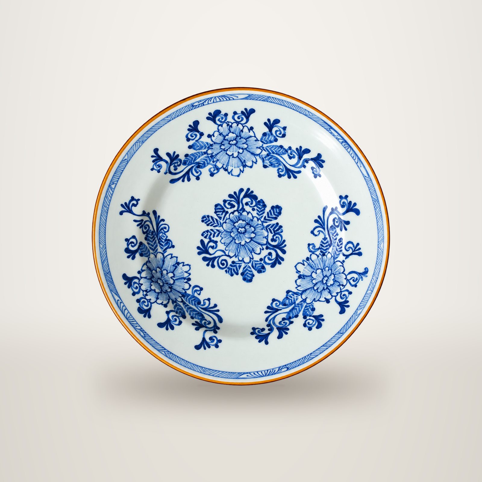 Assiette ancienne en faïence blanche ornée de fleurs bleues peintes à la main, avec un bord brun doré.