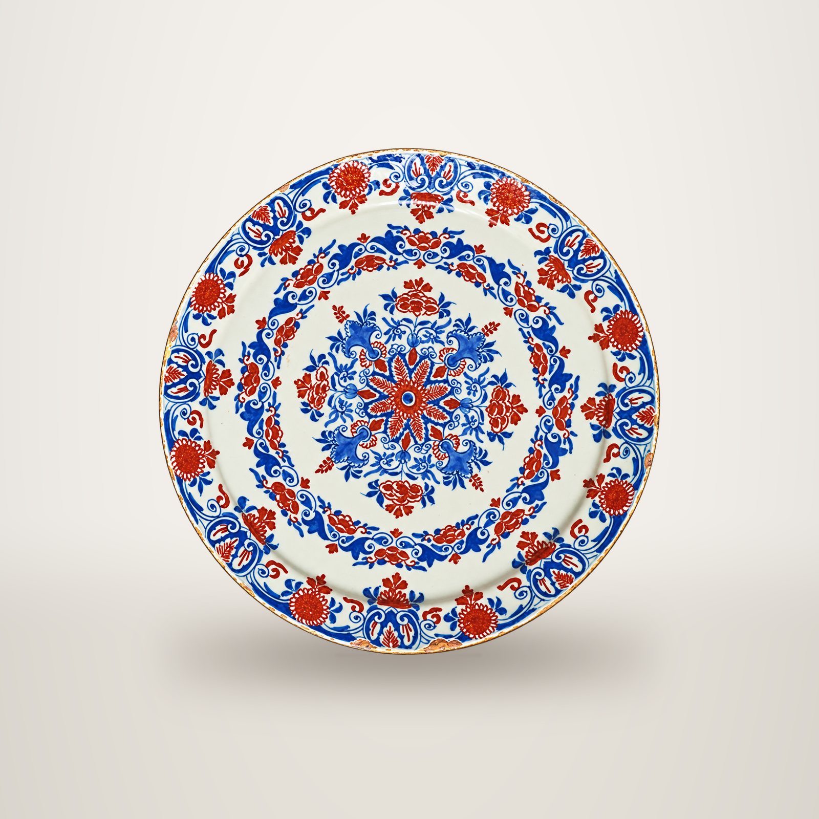 Grande assiette ancienne en faïence ornée de motifs floraux bleus et rouge brique, posée sur un fond de cuir sombre.