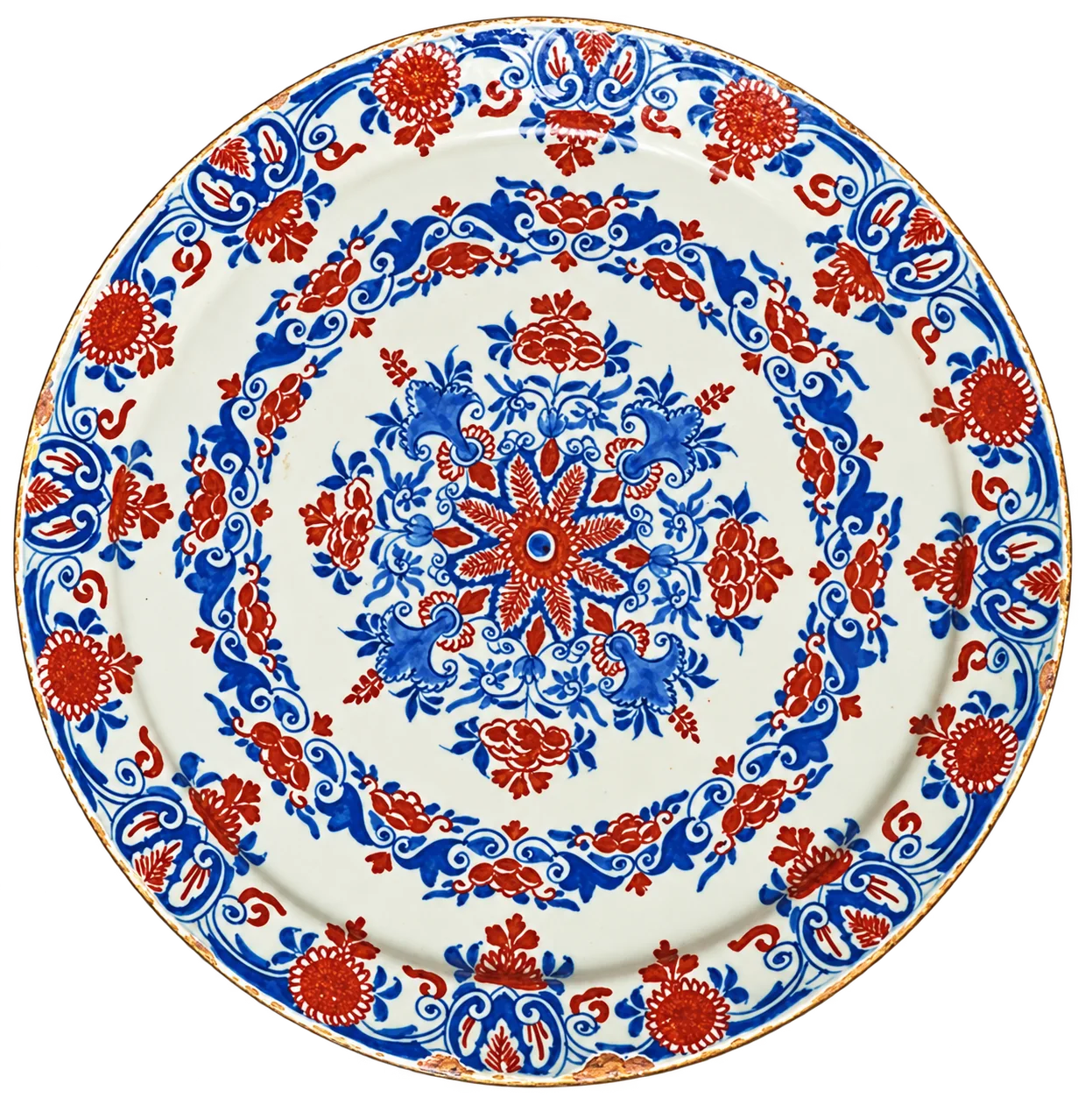 Grande assiette ancienne en faïence ornée de motifs floraux bleus et rouge brique, posée sur un fond de cuir sombre.