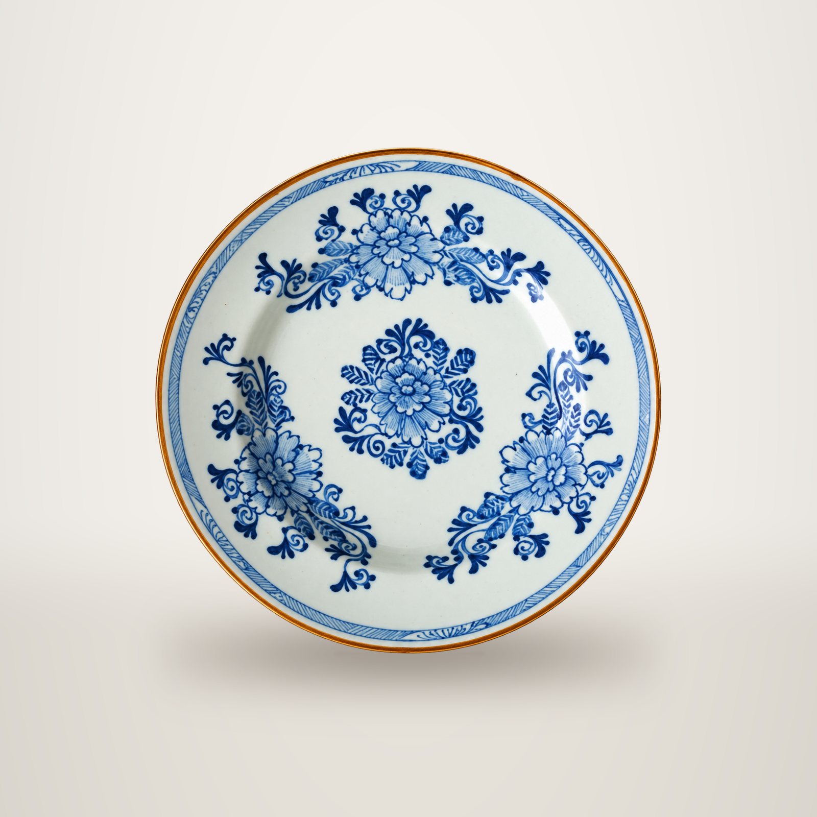 Assiette ancienne en porcelaine blanche ornée de fleurs bleues stylisées et d'un liseré brun sur le bord, photographiée sur fond blanc.