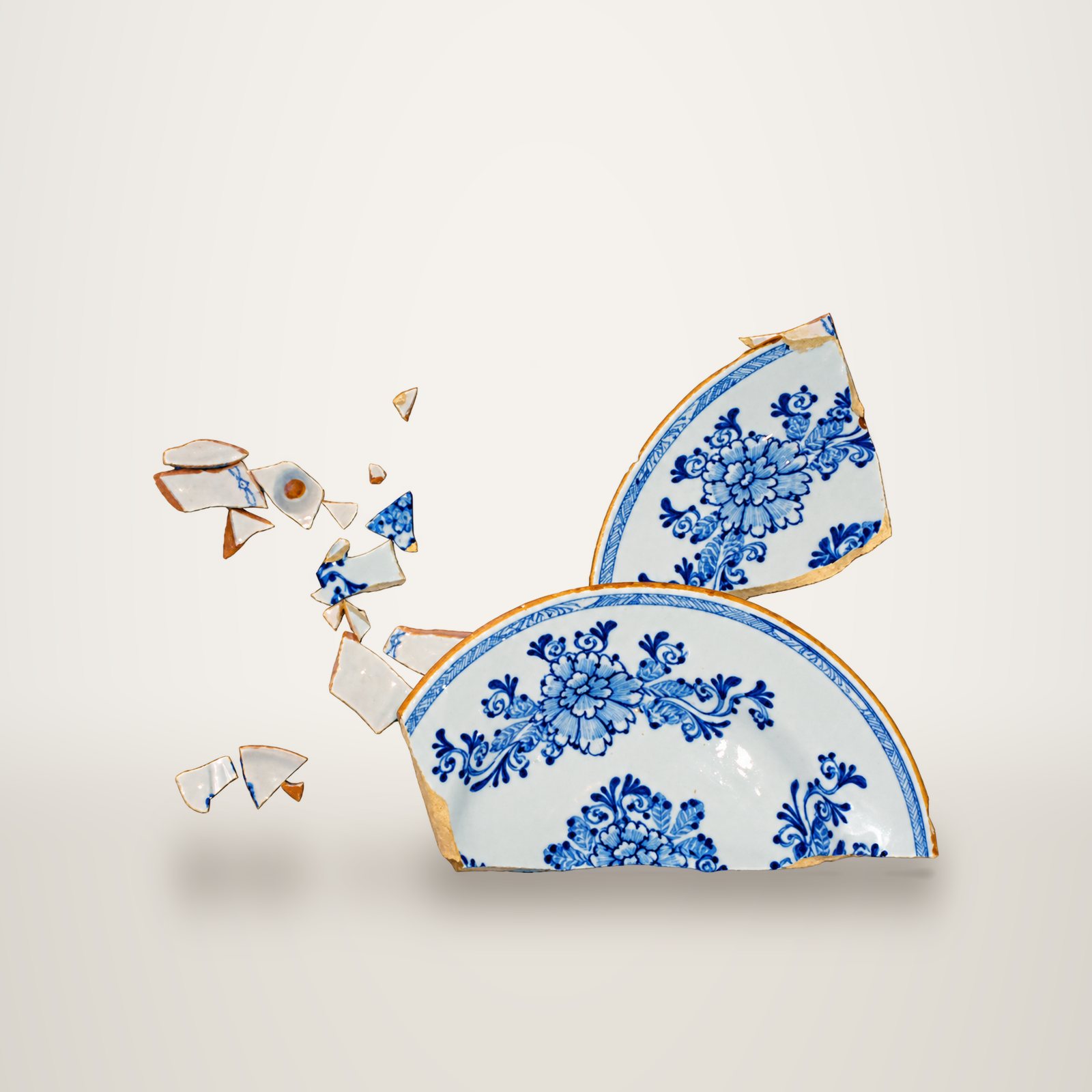 Une assiette ancienne en faïence à décor floral bleu cassée en plusieurs grands fragments et de nombreux petits éclats, sur fond blanc.