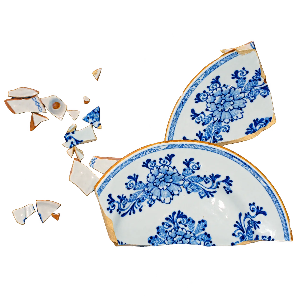 Une assiette ancienne en faïence à décor floral bleu cassée en plusieurs grands fragments et de nombreux petits éclats, sur fond blanc.