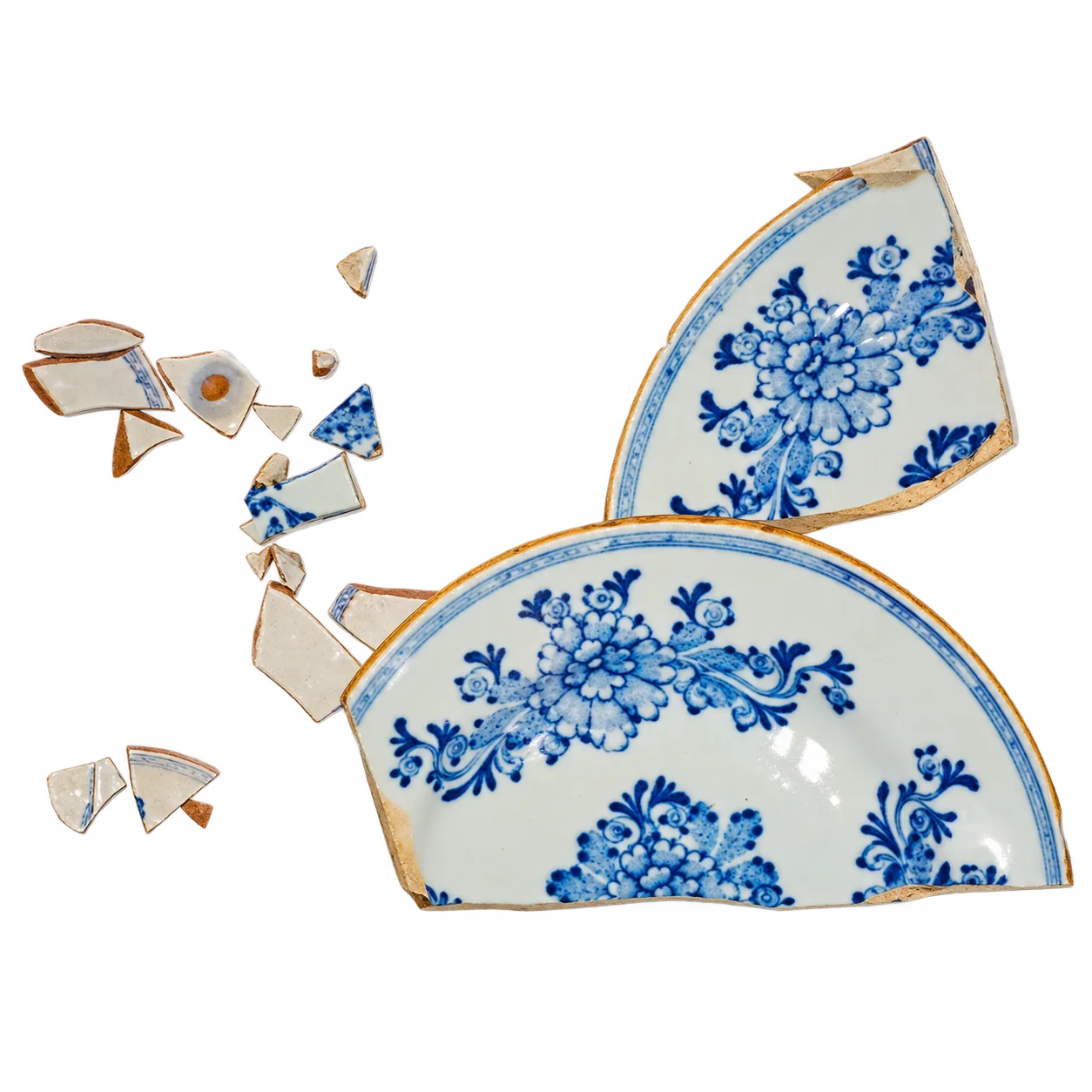 Une assiette ancienne en faïence à décor floral bleu sur fond blanc, brisée en plusieurs grands morceaux et petits éclats, photographiée sur fond blanc uni.