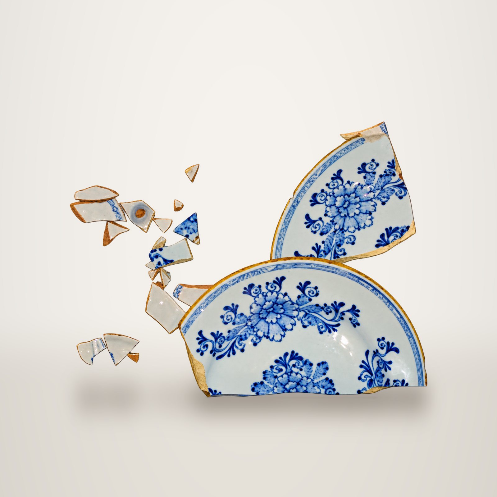 Une assiette ancienne en faïence à motifs floraux bleus sur fond blanc, brisée en plusieurs grands fragments et de petits éclats.