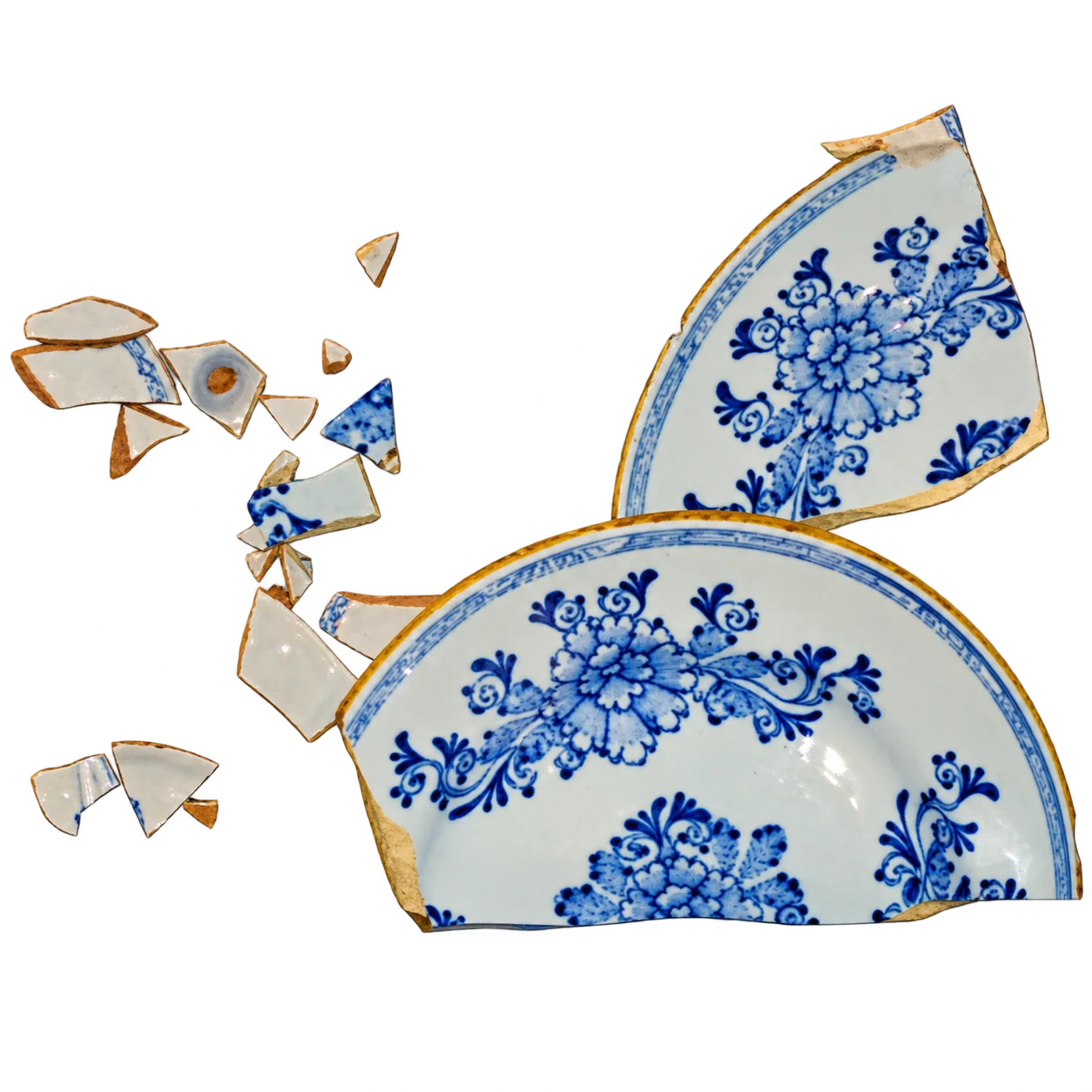 Une assiette ancienne en faïence à motifs floraux bleus sur fond blanc, brisée en plusieurs grands fragments et de petits éclats.
