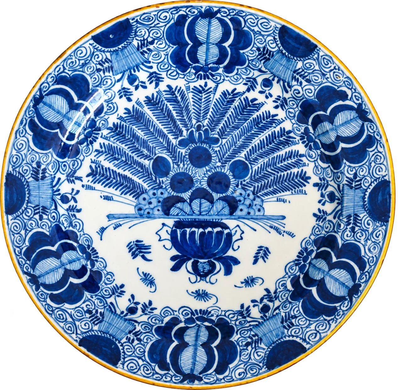 Assiette ancienne en faïence de Delft à motifs bleus et blancs, avec un bouquet de plumes de paon au centre et des fleurs stylisées sur le bord.