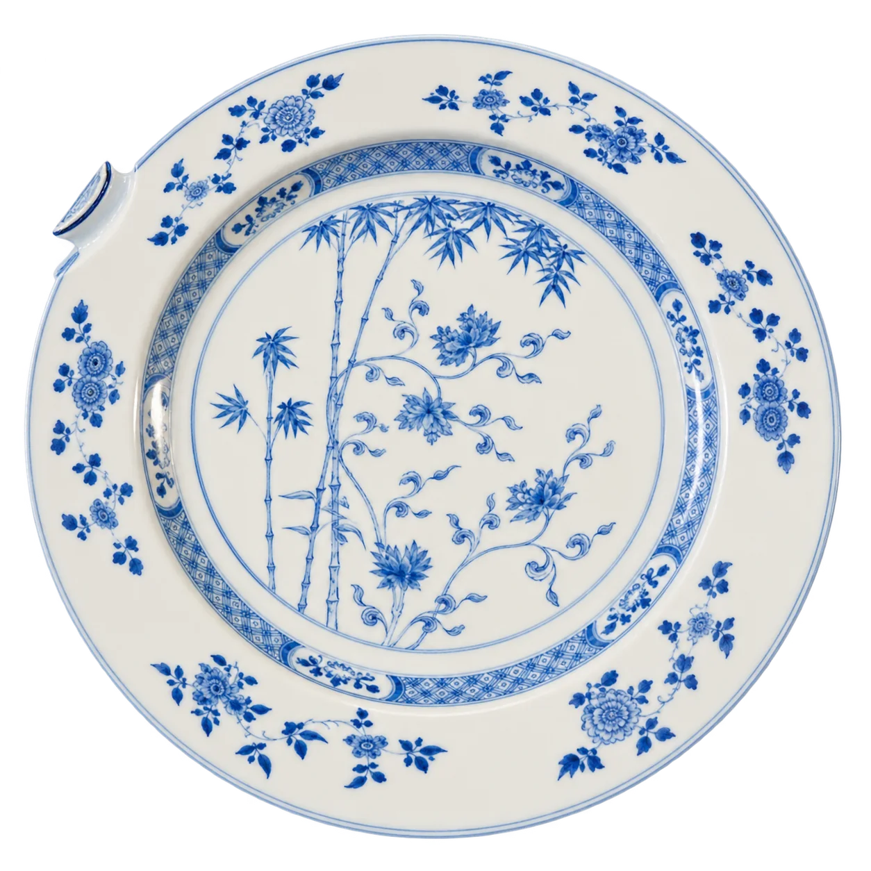 Une assiette ancienne en porcelaine blanche ornée de bambous et de motifs floraux bleus, avec un petit éclat sur le bord, photographiée sur fond blanc.