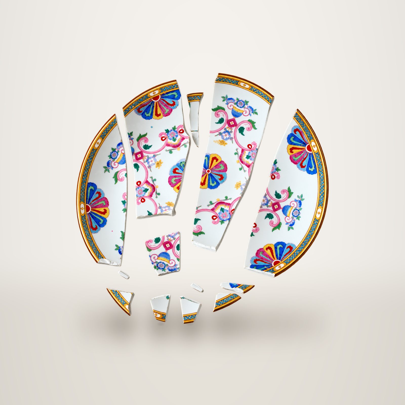 Une assiette en porcelaine à motifs floraux colorés, cassée en plusieurs fragments disposés en cercle sur fond blanc.