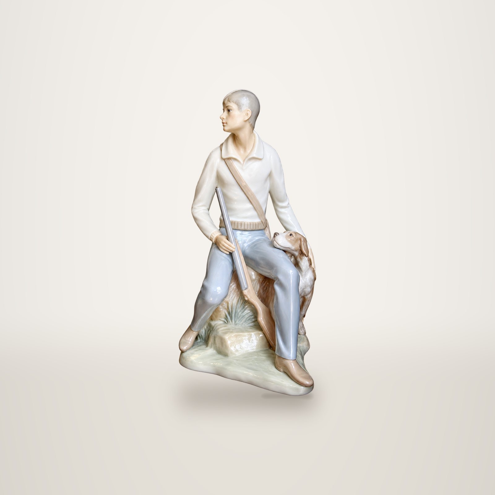 Figurine en porcelaine aux tons pastel représentant un chasseur assis sur un rocher, un fusil à la main, avec un chien à ses côtés.