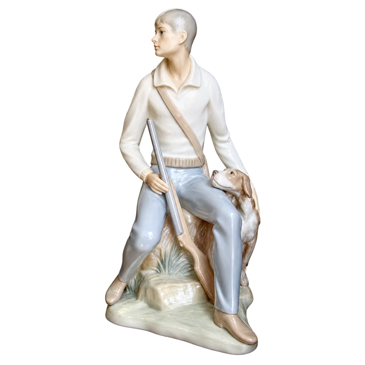 Figurine en porcelaine aux tons pastel représentant un chasseur assis sur un rocher, un fusil à la main, avec un chien à ses côtés.