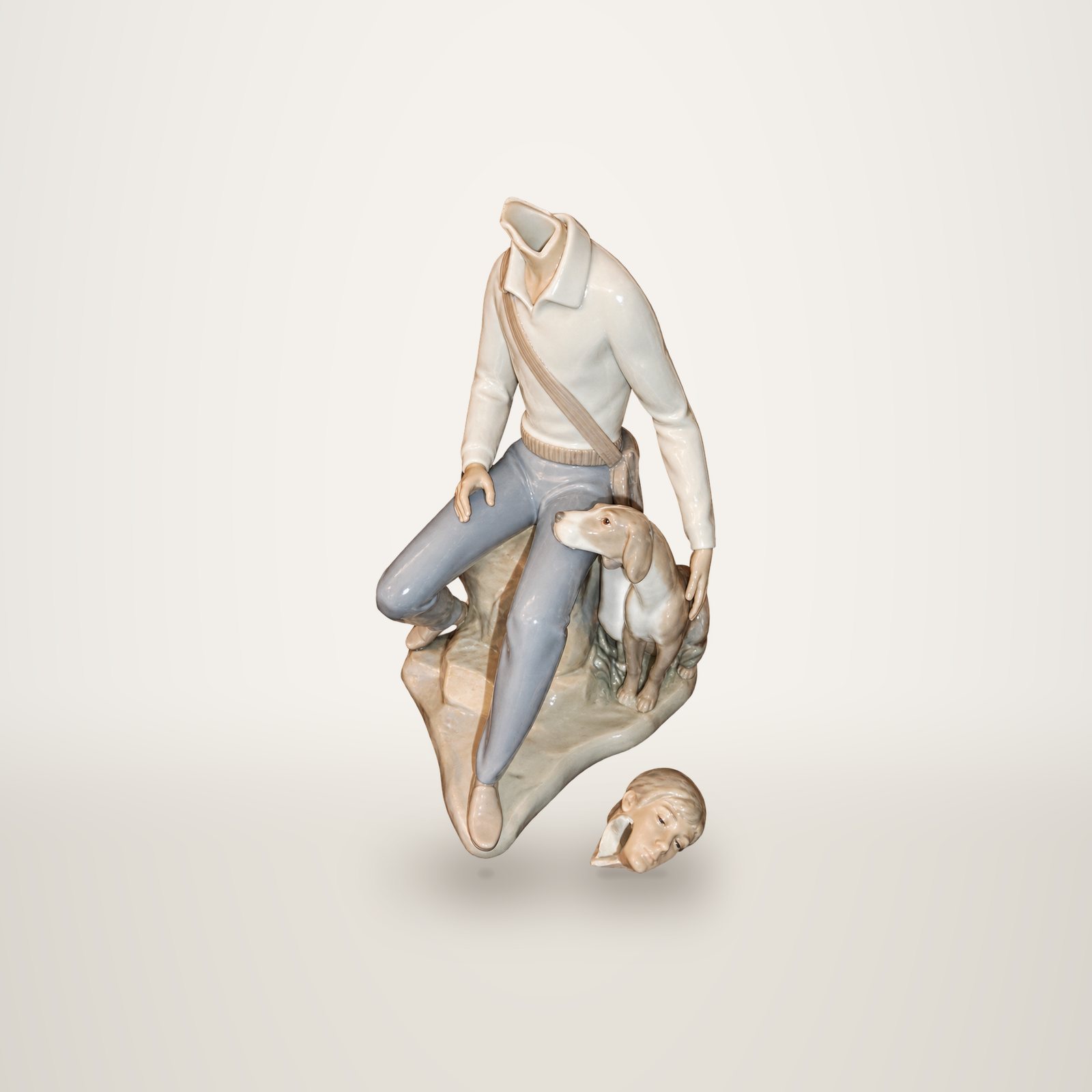 Figurine en porcelaine d'un homme assis sur un rocher avec son chien, dont la tête cassée est posée à côté, sur fond blanc.