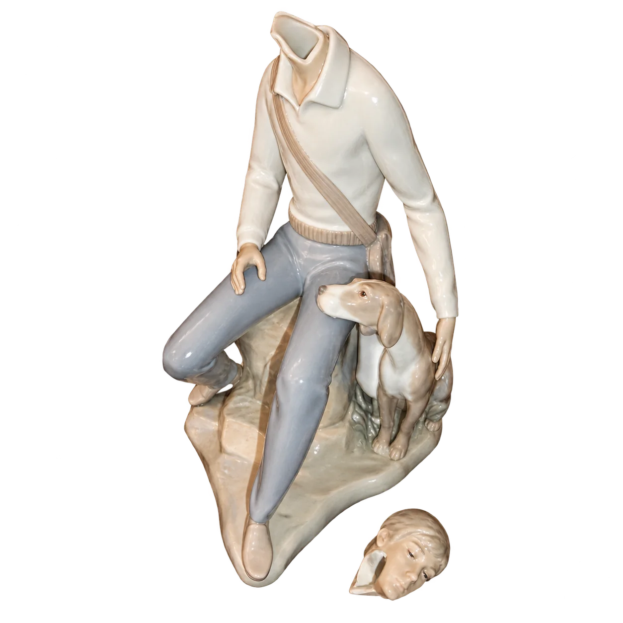 Figurine en porcelaine d'un homme assis sur un rocher avec son chien, dont la tête cassée est posée à côté, sur fond blanc.