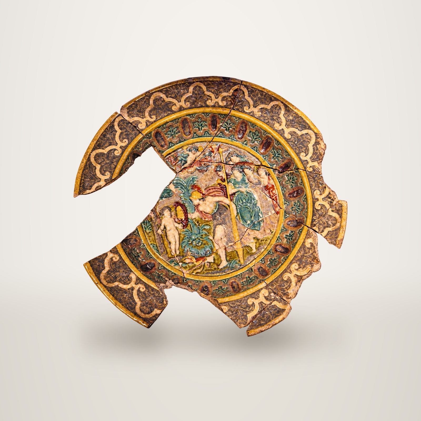 Fragment d'un plat ancien en céramique émaillée, orné d'une scène en relief colorée avec des personnages et d'une bordure à motifs dorés, photographié sur fond blanc.