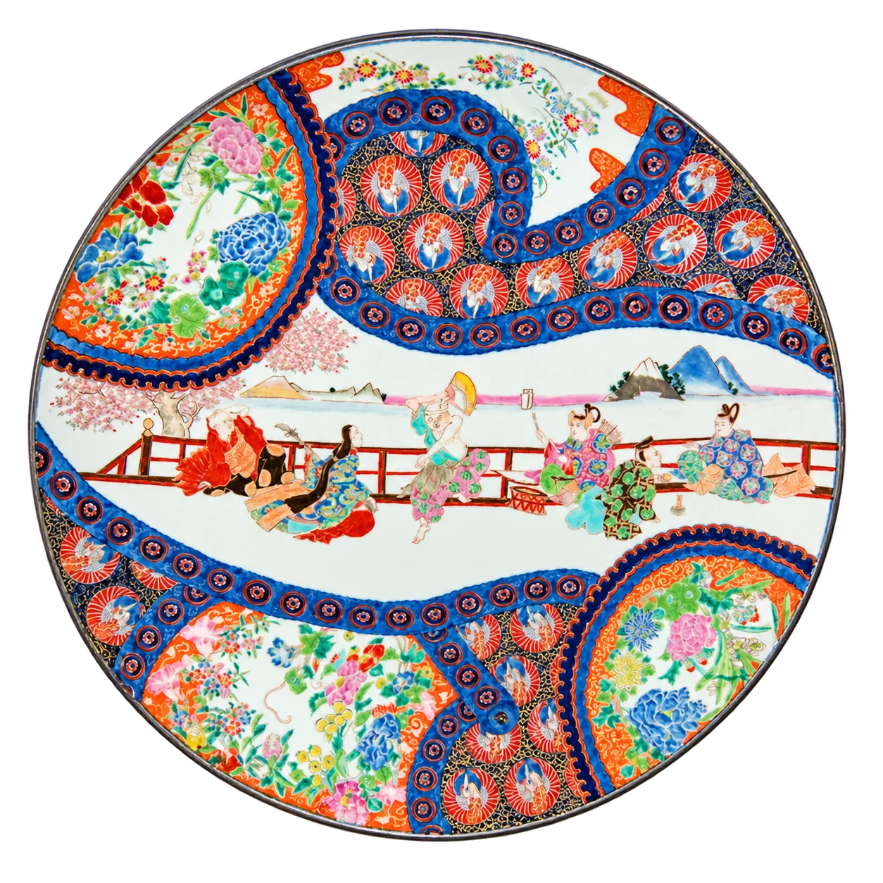 Grand plat rond en porcelaine japonaise orné de personnages près d'une balustrade, de motifs floraux colorés et de bordures bleues et rouges.