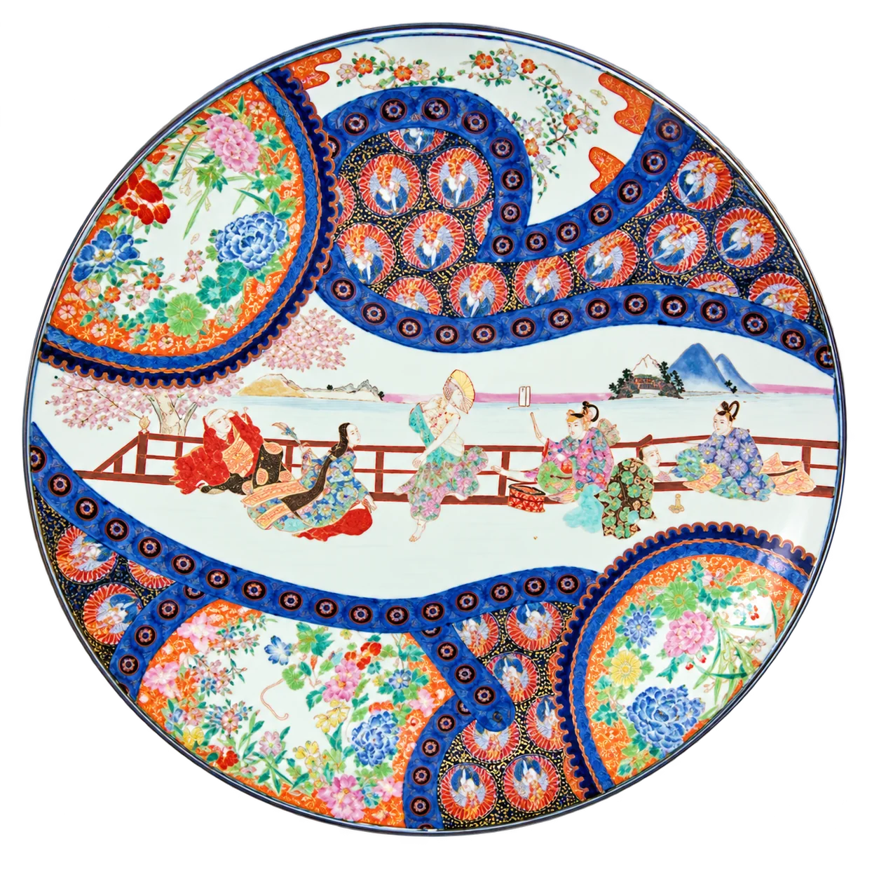 Grand plat rond en porcelaine aux motifs japonais colorés, avec une scène de personnages sur une terrasse et des médaillons de fleurs bleus et orange.