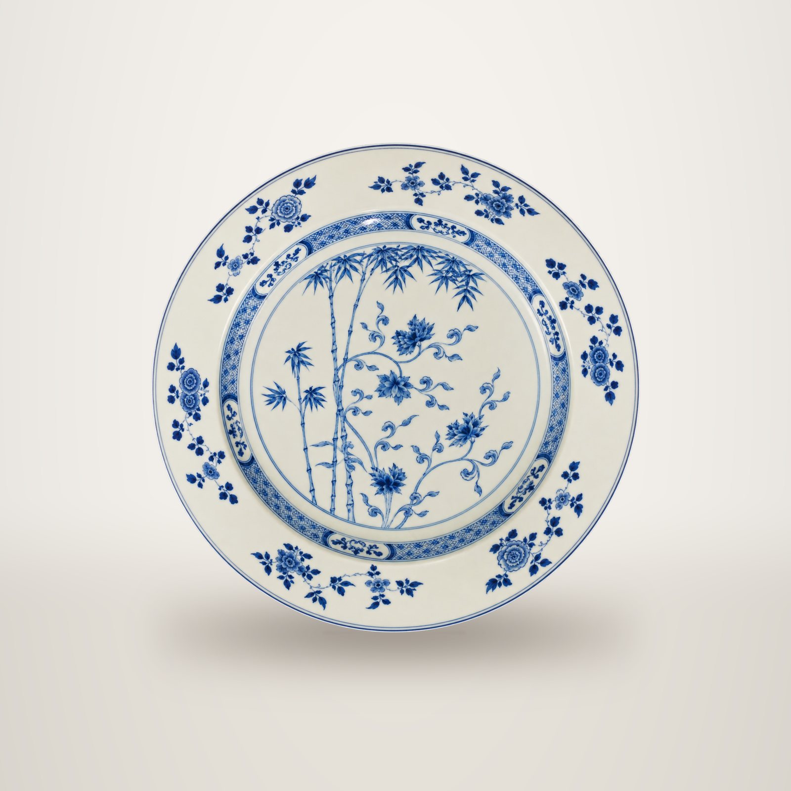 Plat rond en porcelaine blanche orné d'un décor bleu de bambous, de branches fleuries et d'une bordure de motifs floraux, photographié sur fond blanc.