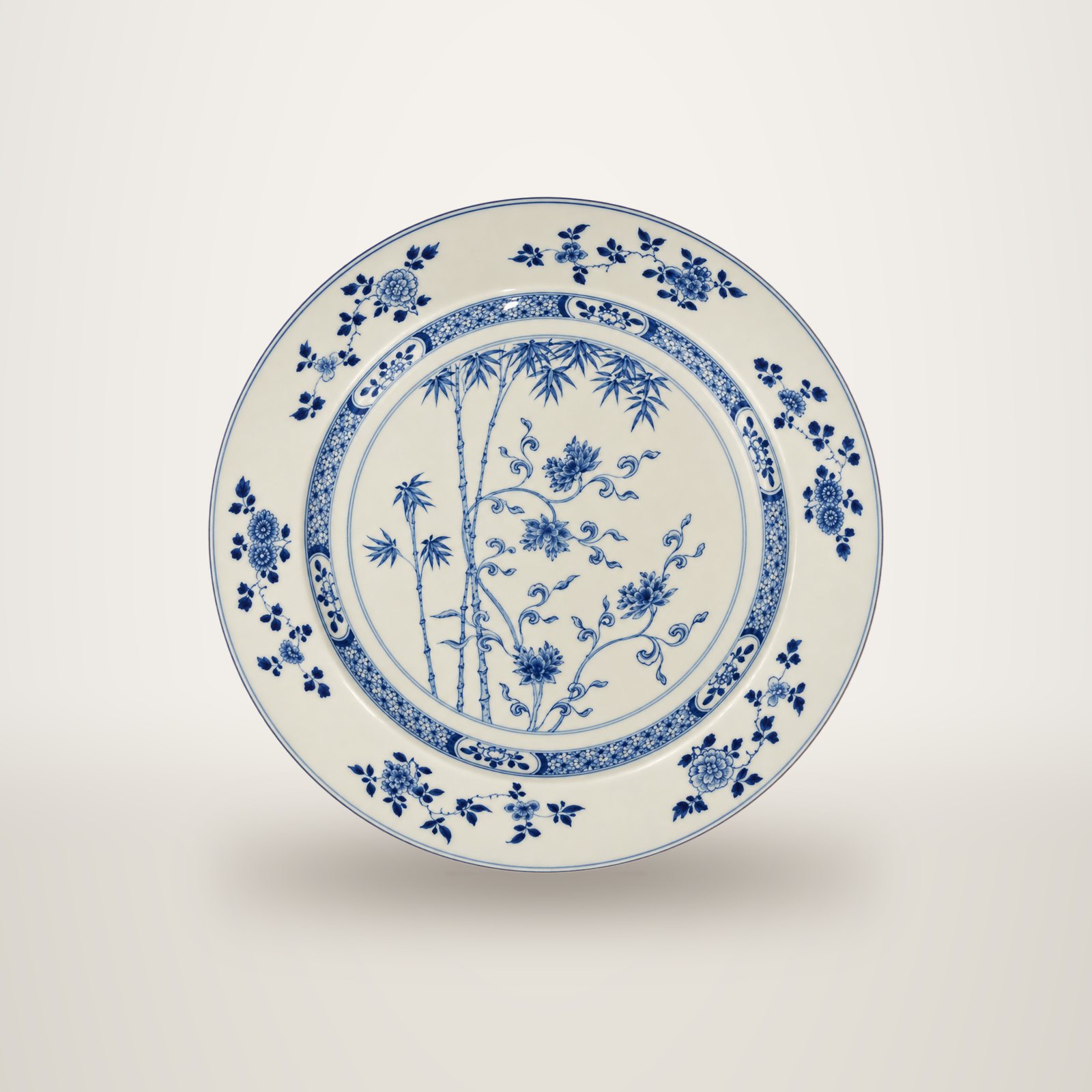Grand plat rond en porcelaine blanche décoré en bleu de bambous et de fleurs, avec une bordure ornée de motifs floraux.