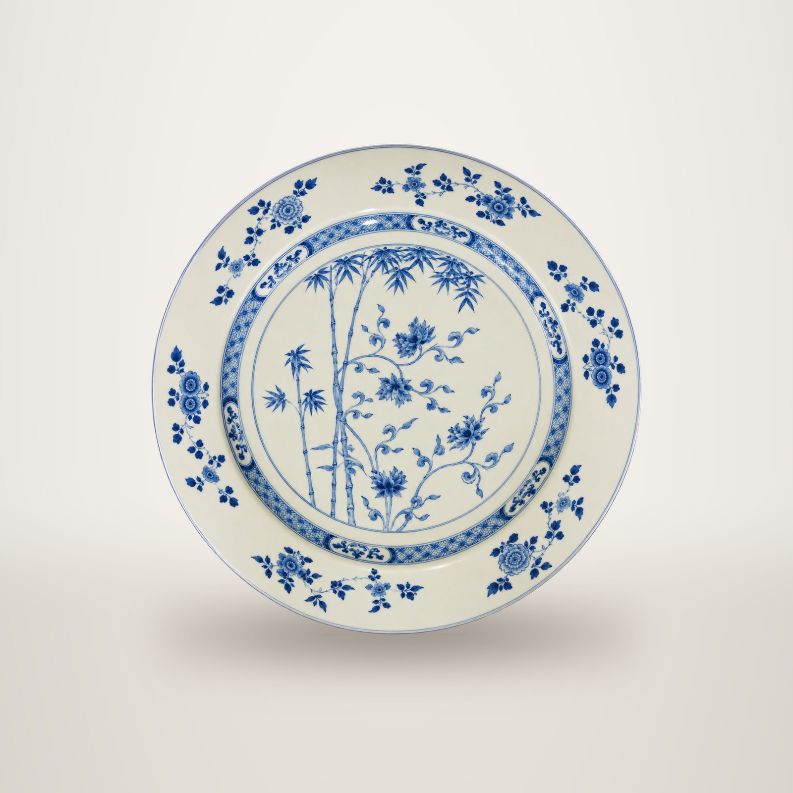 Un grand plat rond en porcelaine blanche orné de bambous et de fleurs peints en bleu, avec une bordure à motifs floraux.