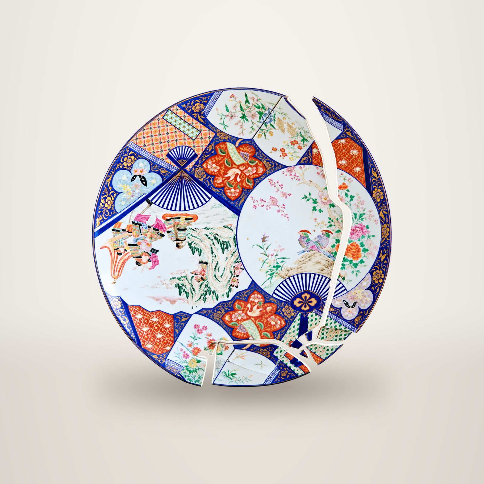 Un grand plat en porcelaine ancienne à décor d'éventails, de fleurs et d'oiseaux dans des tons bleu, rouge et or, fendu en plusieurs fragments.
