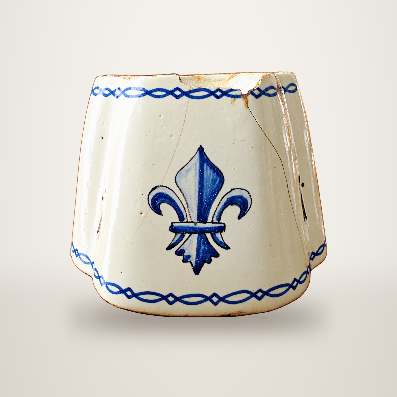 Pot ancien en faïence blanche, ébréché au bord, orné d'une fleur de lys bleue et de frises bleues tressées.