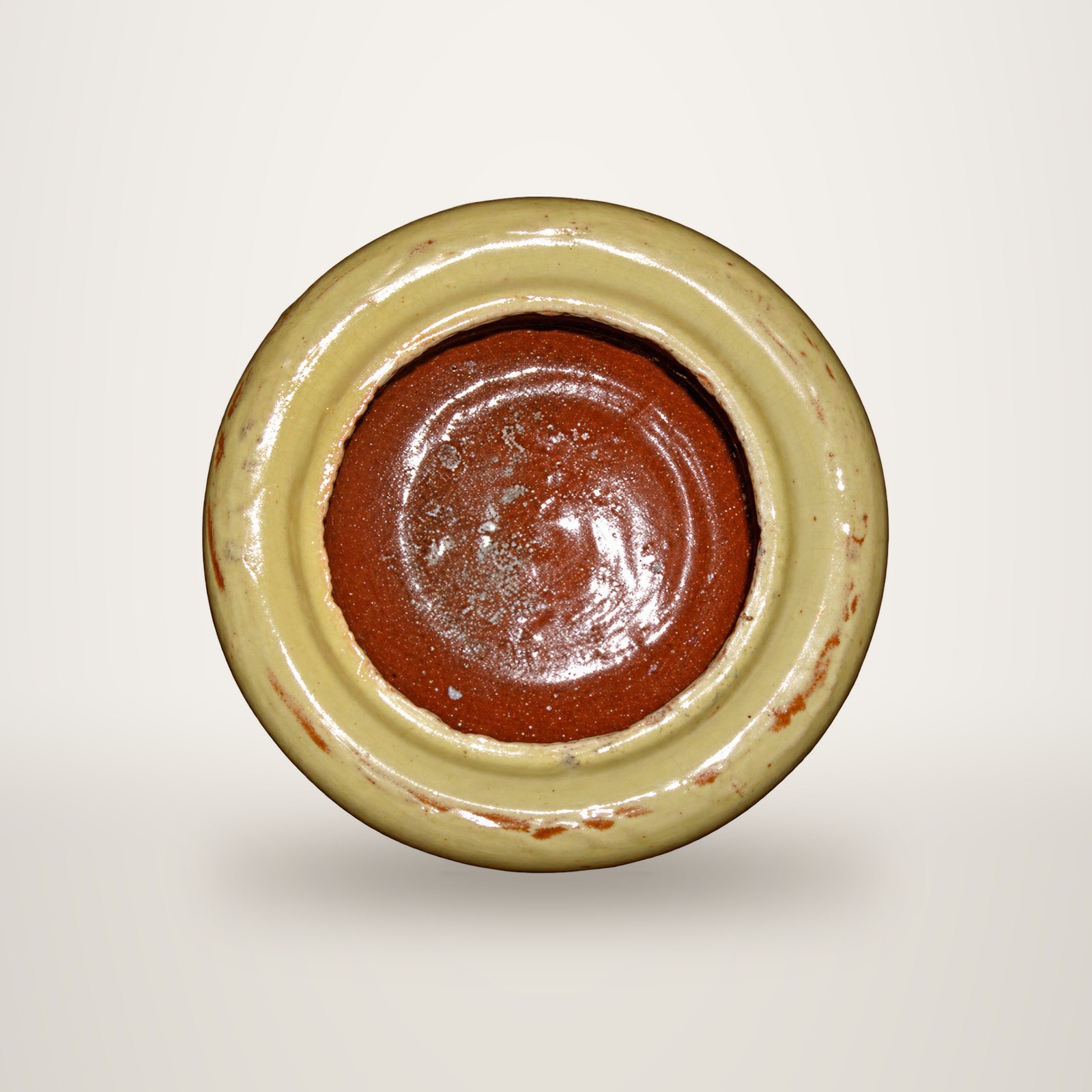 Vue de dessus d'un pot en terre cuite vernissée au bord beige épais et à l'intérieur brun-rouge brillant, sur fond blanc.