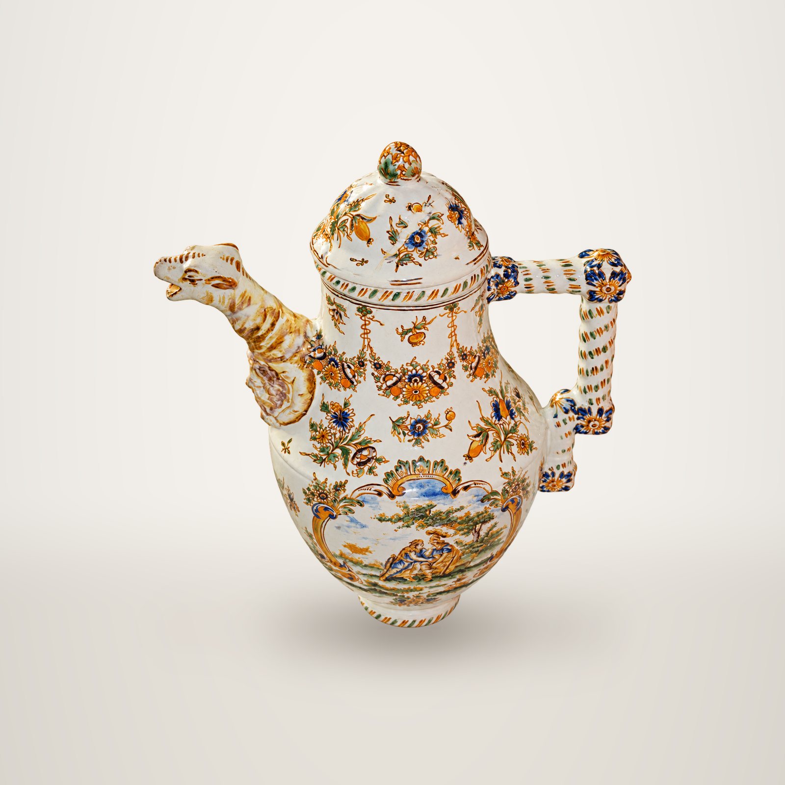 Verseuse ancienne en faïence blanche aux motifs de fleurs colorées, avec un bec en forme de tête d'animal et une anse torsadée.